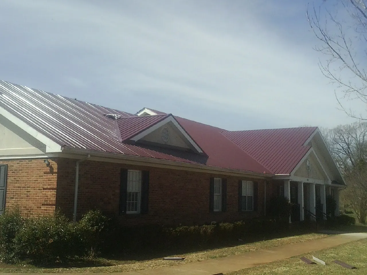 Red metal roof with gabled entries on a long brick building, from a Hail Damage Roof Repair job in Galloway
