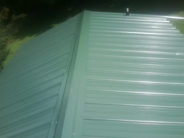 New green metal panels meeting at the ridge of a roof — Flat Roof Repair work by our crew in Galloway