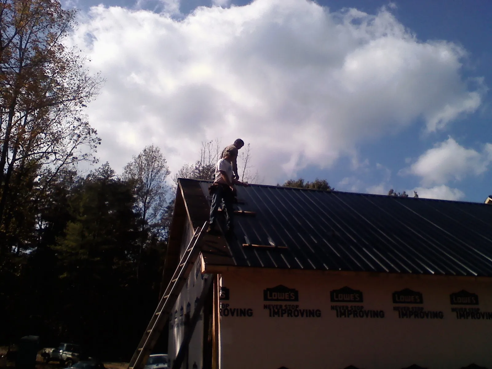 Roofer fastening dark metal panels high against a cloudy sky, from a Roof Inspection job in Galloway